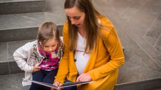 A pregnant mother reading a book for her daughter.